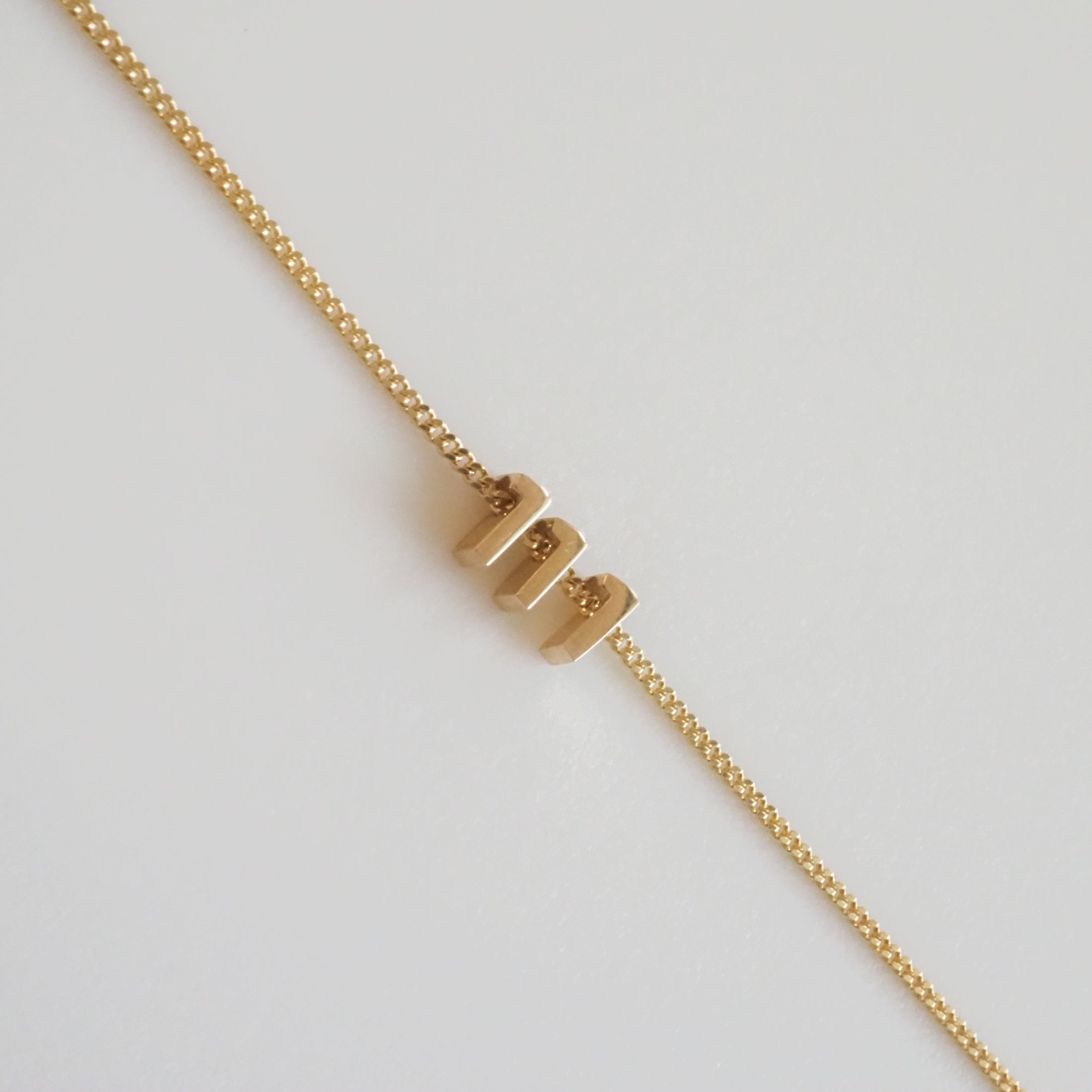 Gold bracelet with delicate chain and three modern rectangular links, elegantly positioned on a plain background. Luxury jewellery.