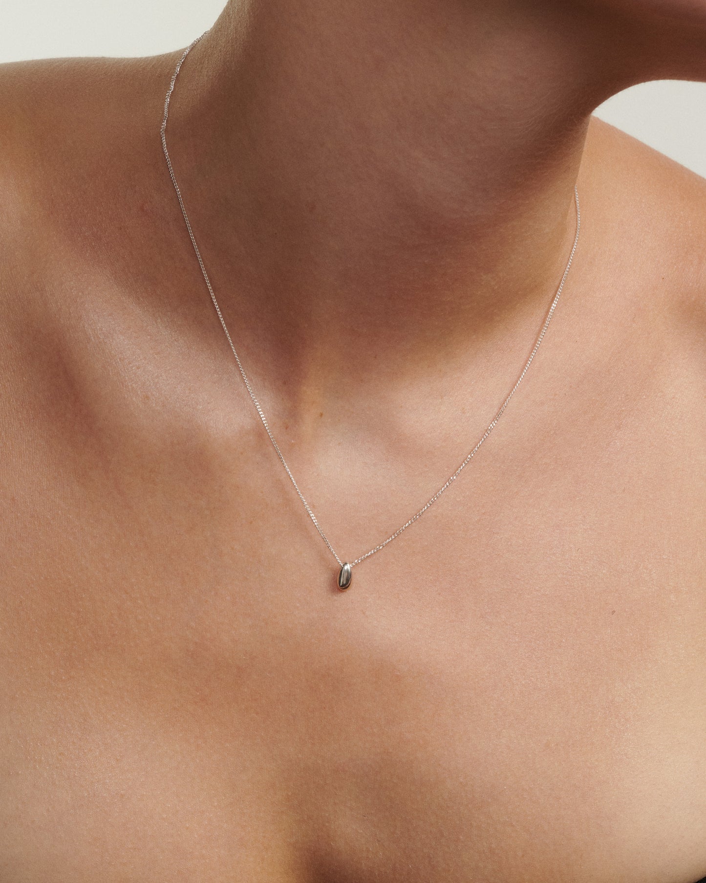 Necklace with a small pendant on a person's neck against a neutral background
