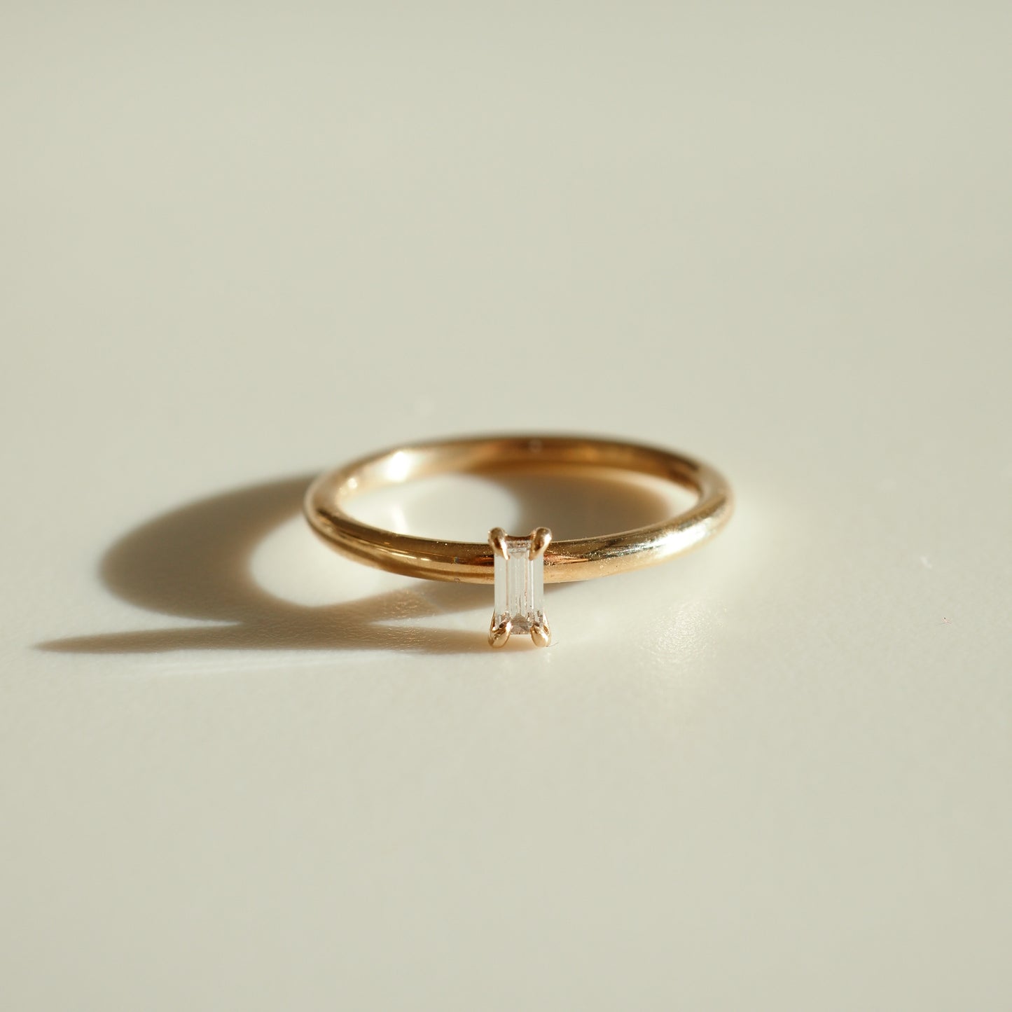 Elegant gold ring featuring a vertically-set baguette diamond, casting a soft shadow on a light background. Ideal luxury jewellery piece.