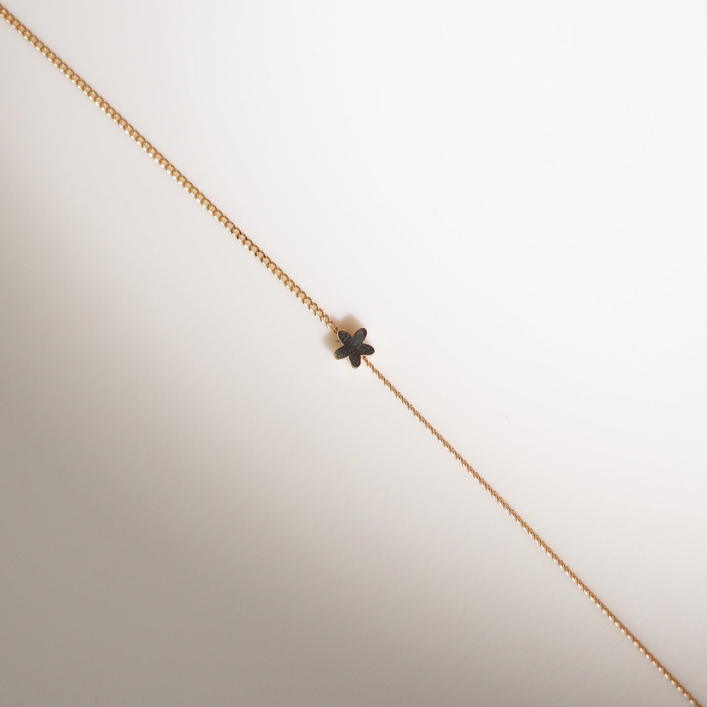 Gold chain necklace featuring a small black four-leaf clover charm. Minimalist luxury jewellery on a light background.