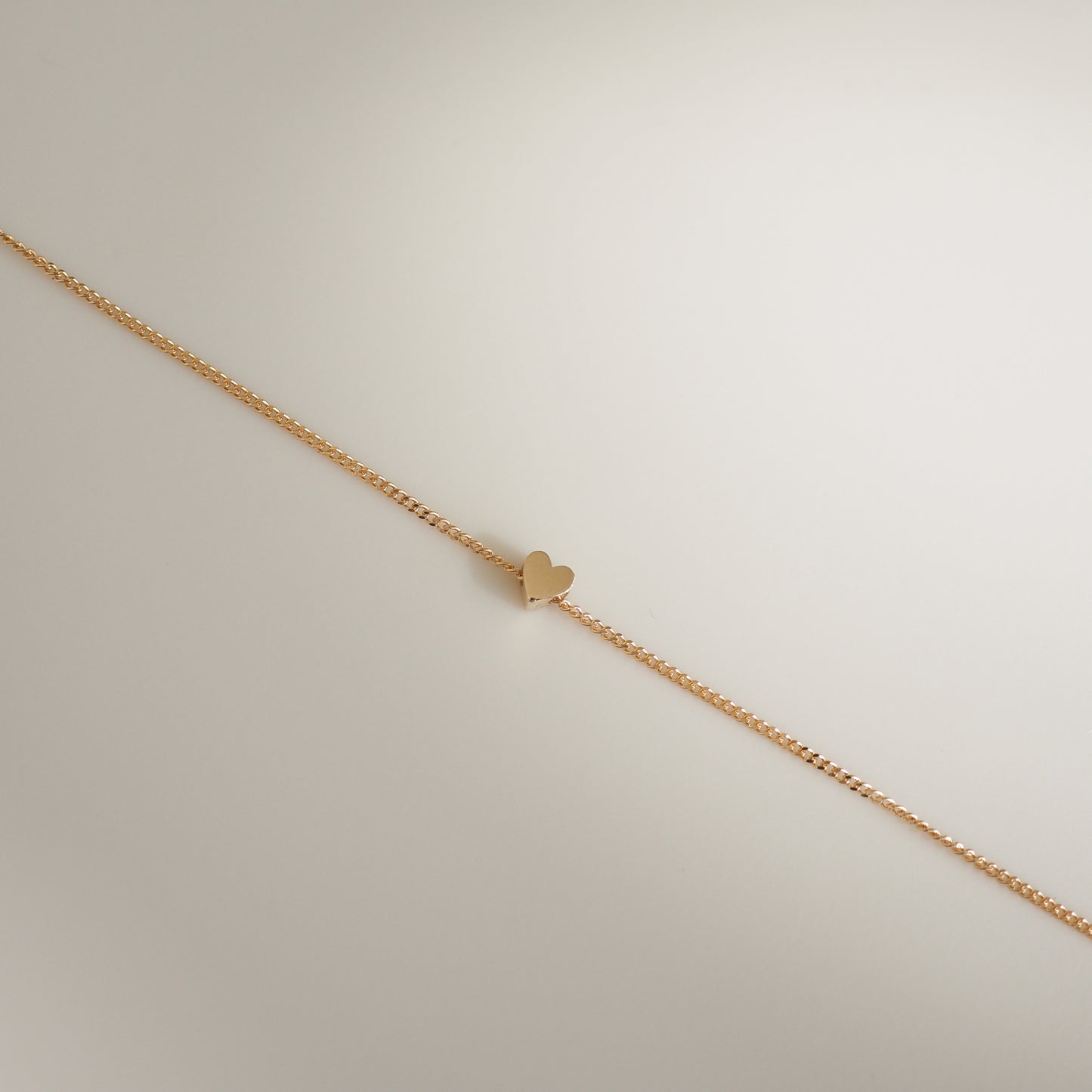 Delicate gold bracelet with a fine chain and tiny heart charm. Elegant jewellery piece on a light background. Perfect for luxury fashion.
