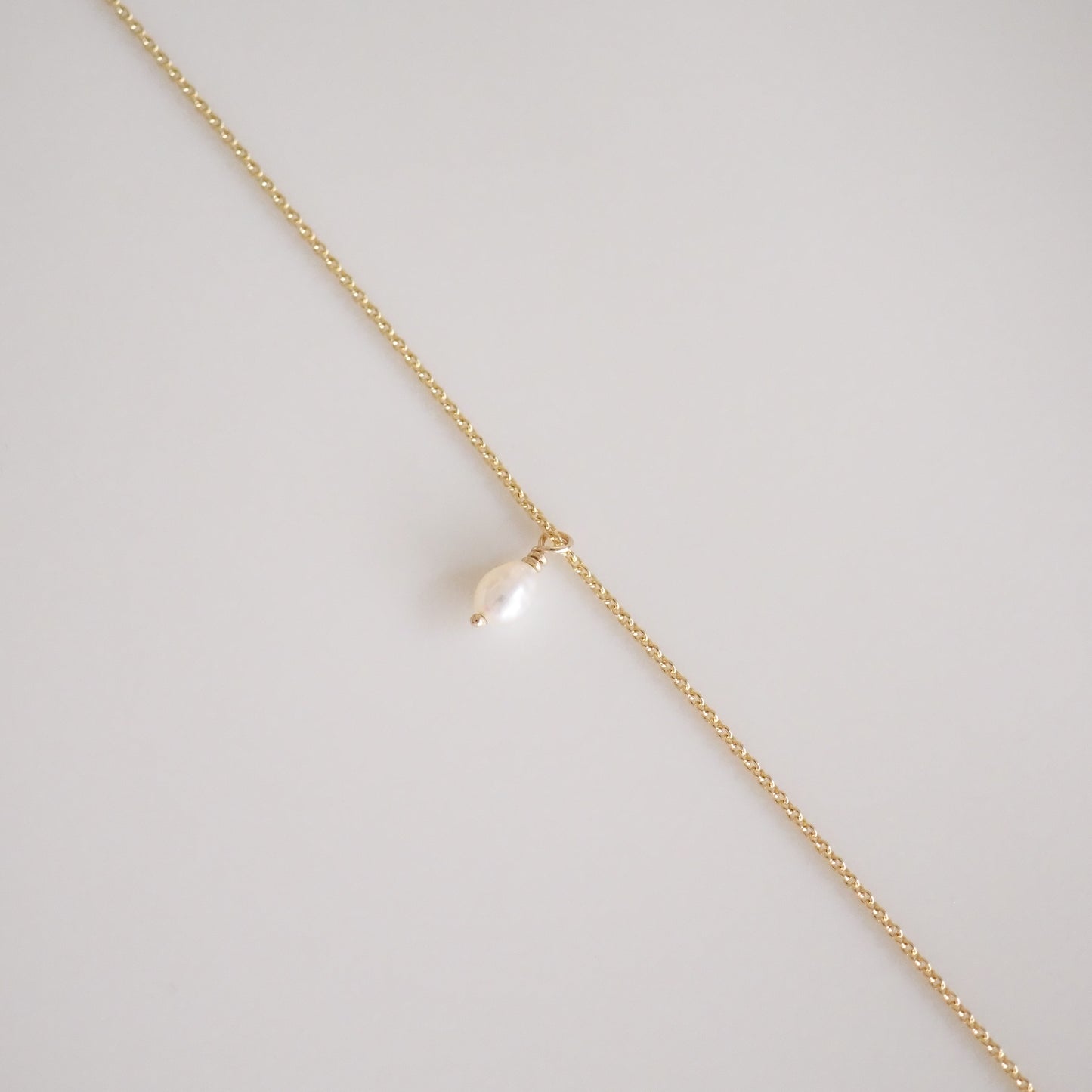 Gold chain necklace with a single white pearl pendant, laid on a light background. Elegant and minimalist jewellery design.