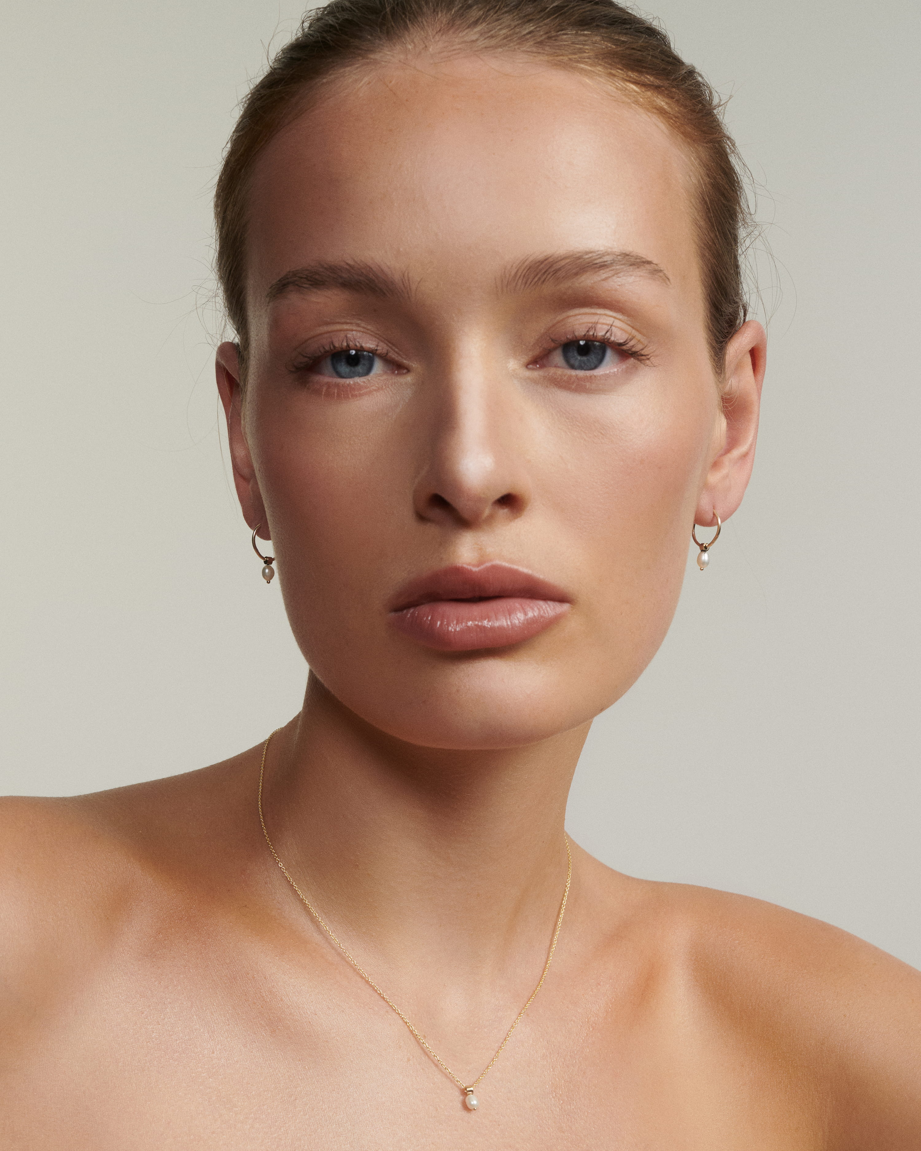 Woman wearing a gold pearl necklace and earrings against a neutral background
