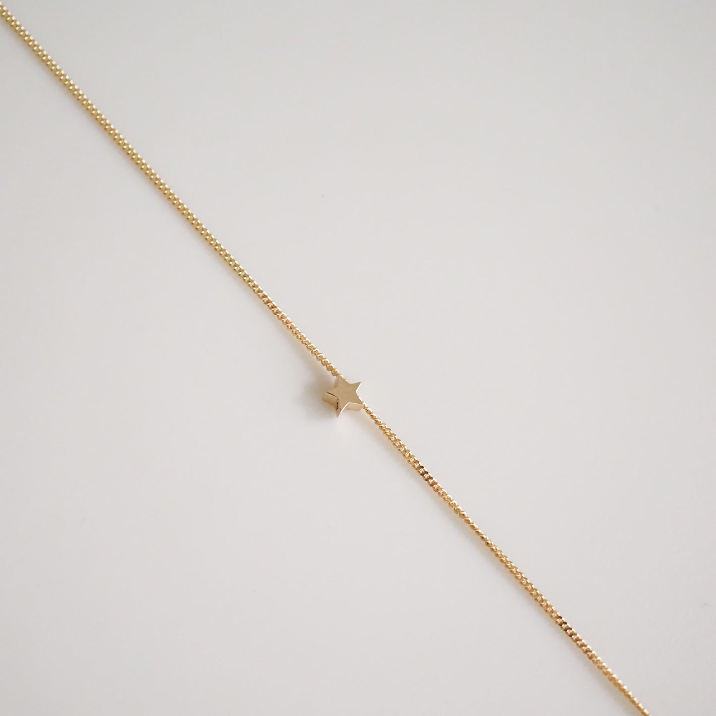 Elegant gold bracelet with a delicate star charm, showcasing minimalist luxury jewellery design on a neutral background.