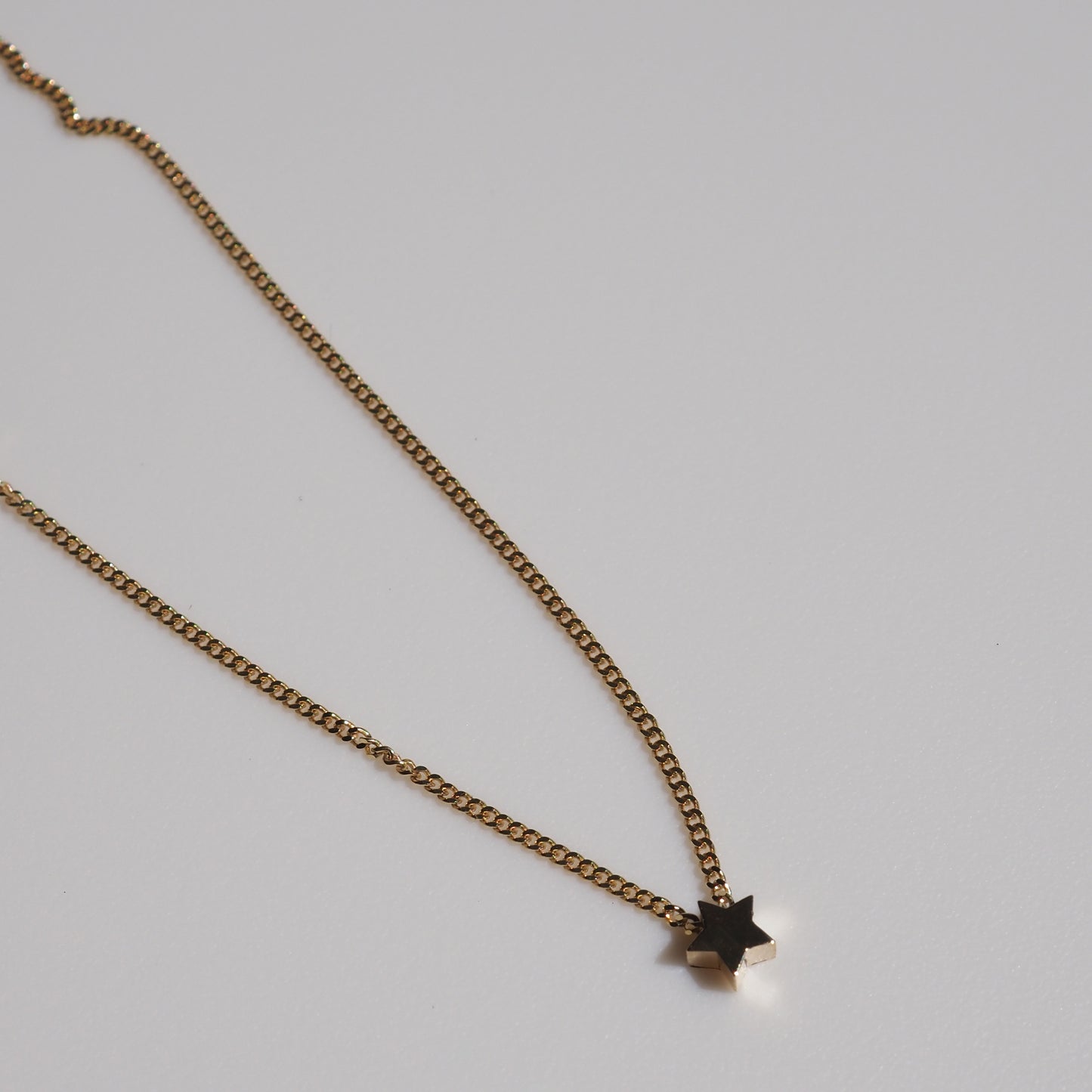 Gold chain necklace featuring a minimalist star pendant against a grey background. Luxury jewellery, elegant design.