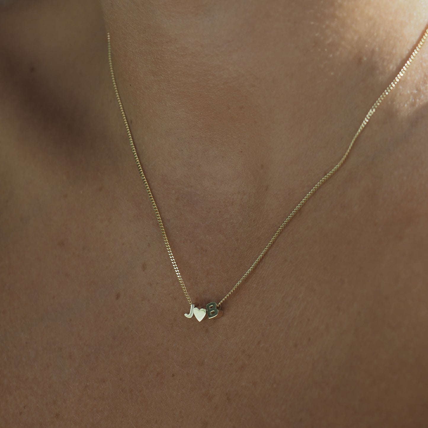 The Tiny Heart Necklace features a gold heart fixed in the centre of a yellow gold chain, personalised with two letters either side of the heart. 