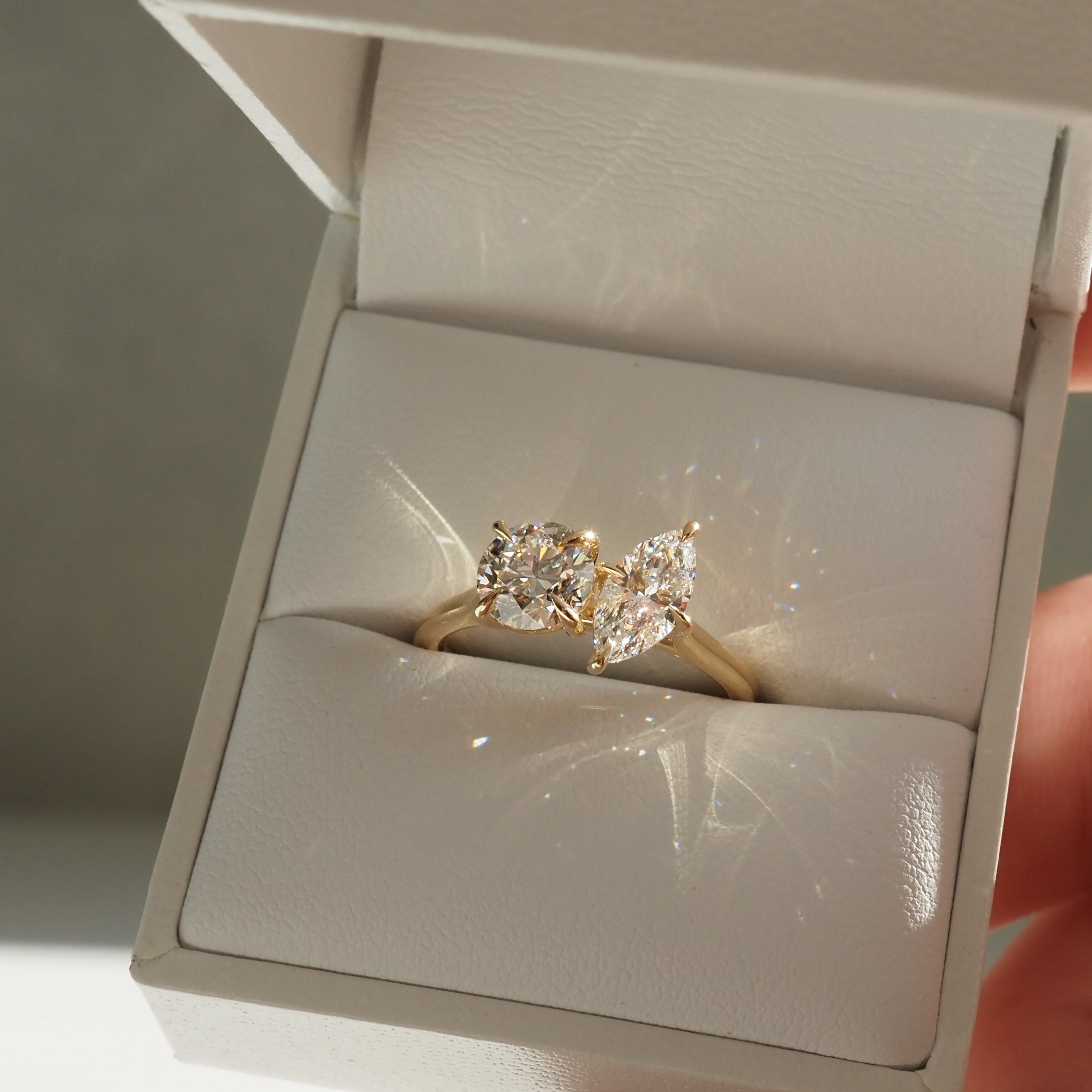 Gold ring with two sparkling diamonds in an open white box, showcasing luxury jewellery design and elegant craftsmanship.