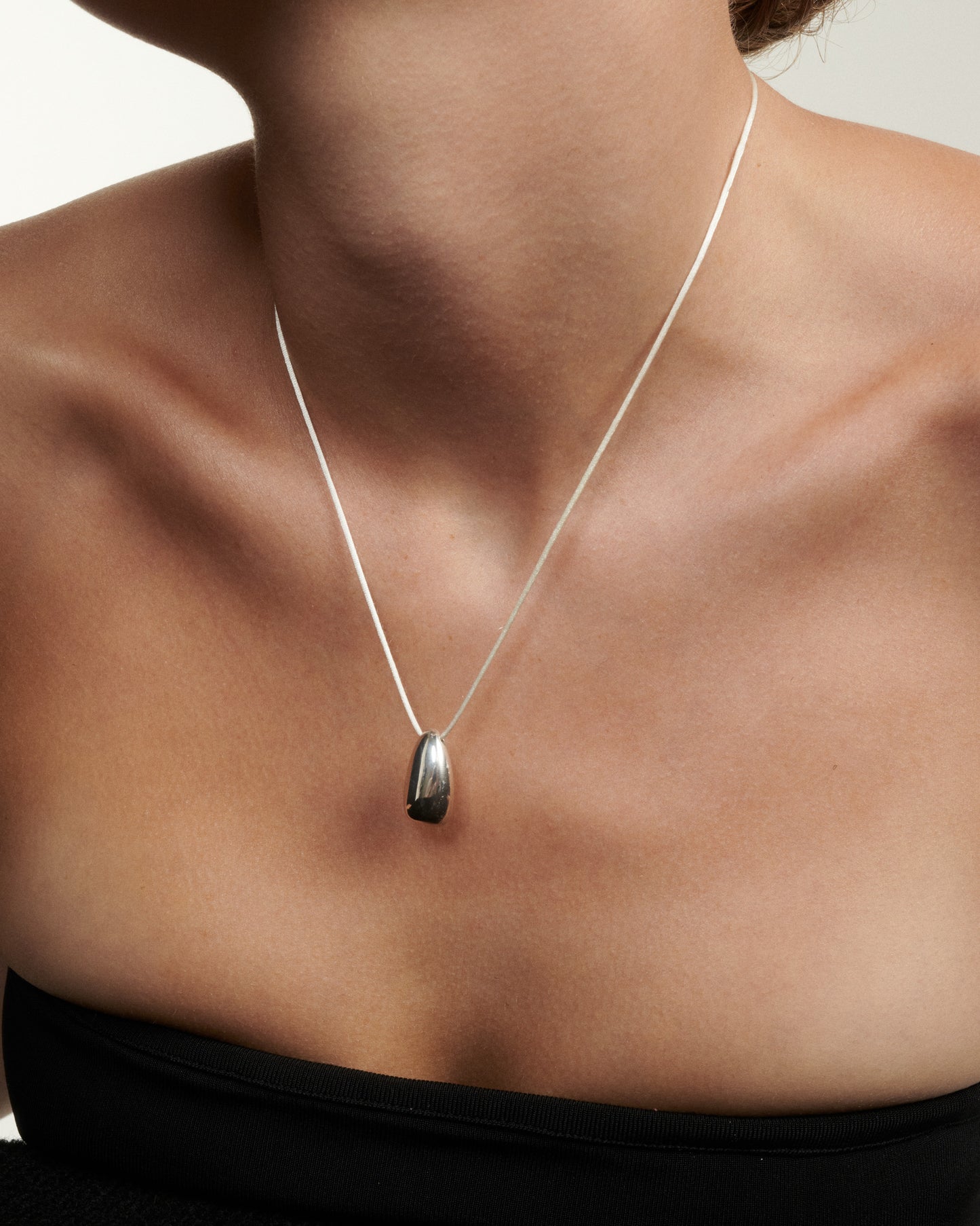 Silver necklace with a pendant on a person wearing a black top against a neutral background