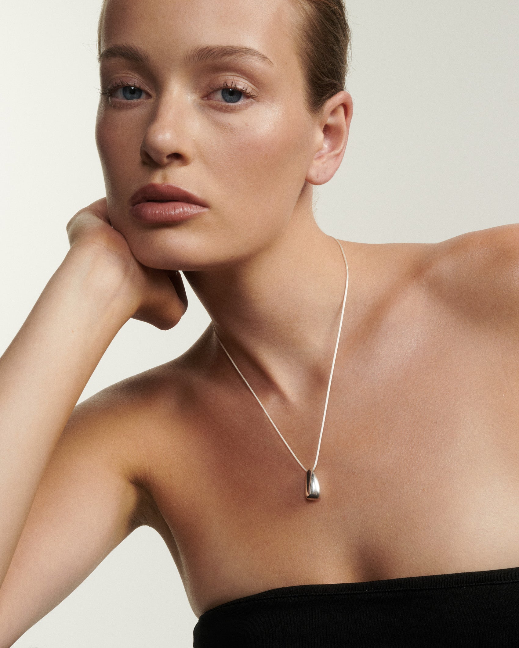 Woman wearing a silver necklace against a plain background [text overlay: Andrea wears the Large Toka Pendant]