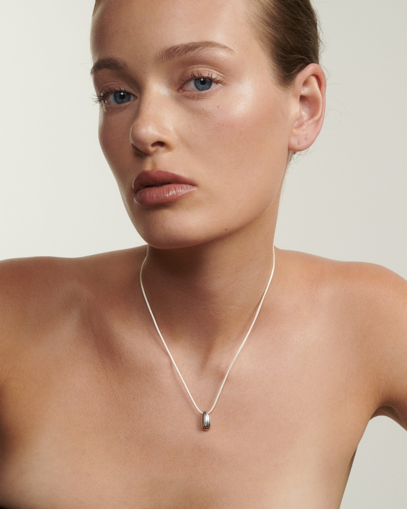 Woman wearing a silver necklace against a plain background [text overlay: Andrea wears the Small Toka Pendant]