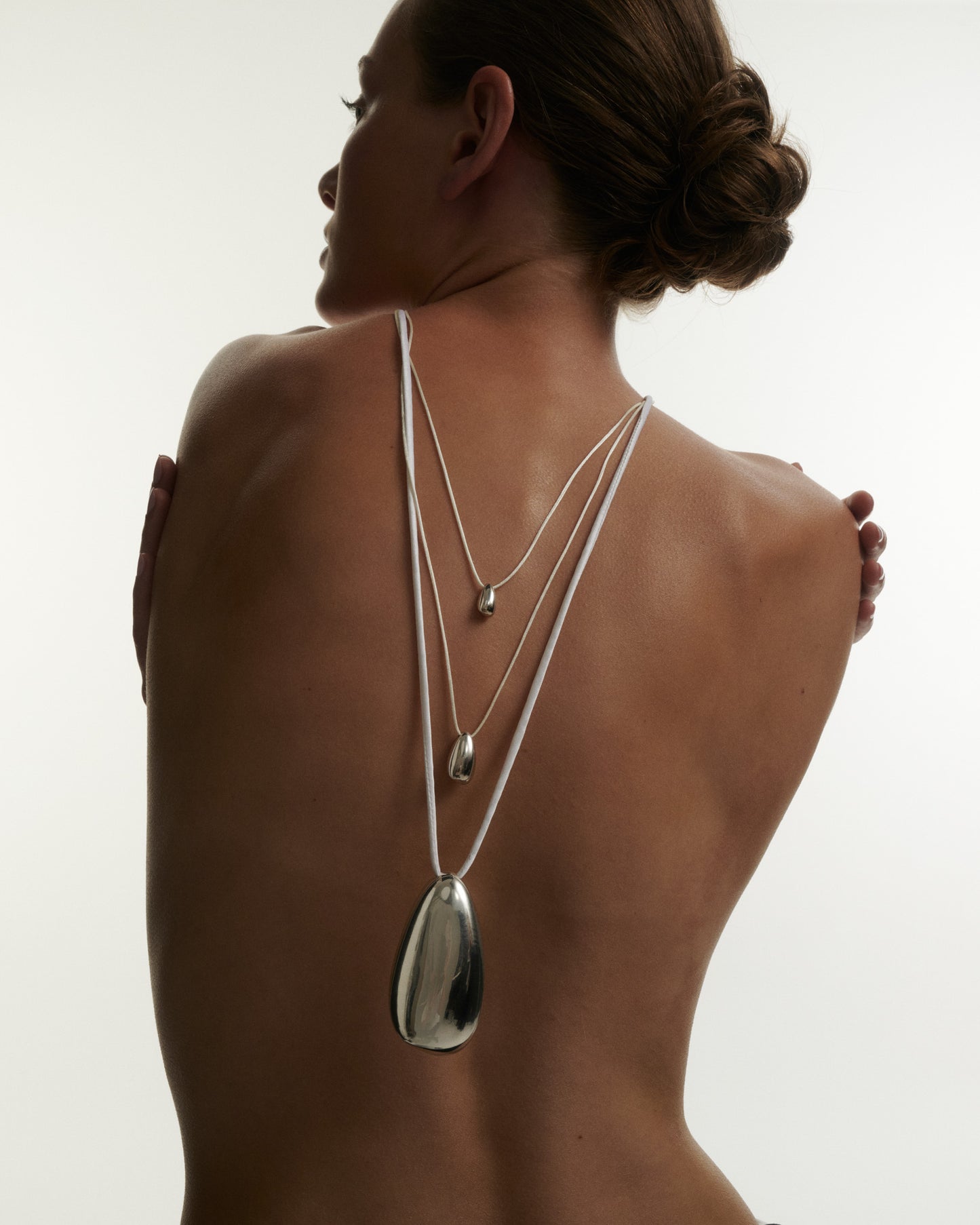 Woman wearing a silver necklace with a pendant on a plain background