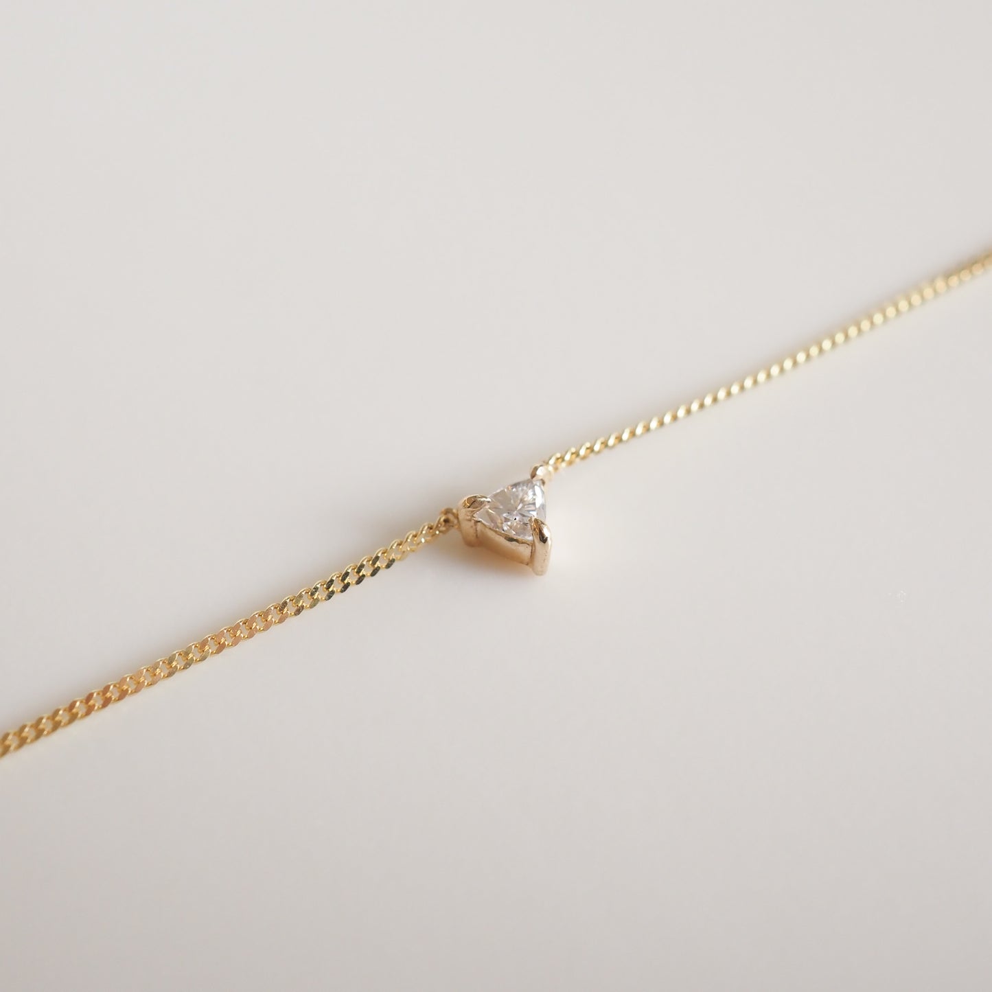 Gold chain necklace with a single, small triangle diamond pendant set in a minimalist style on a plain background.