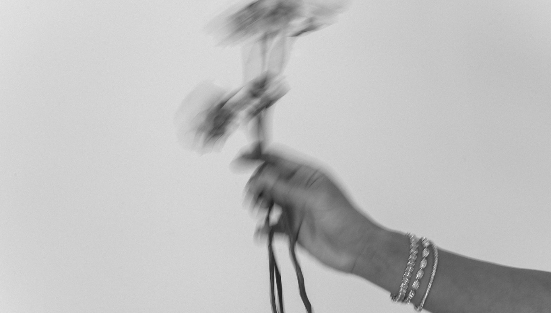 A hand adorned with elegant bracelets holding blurred flowers against a plain background. Luxury jewellery and style concept.