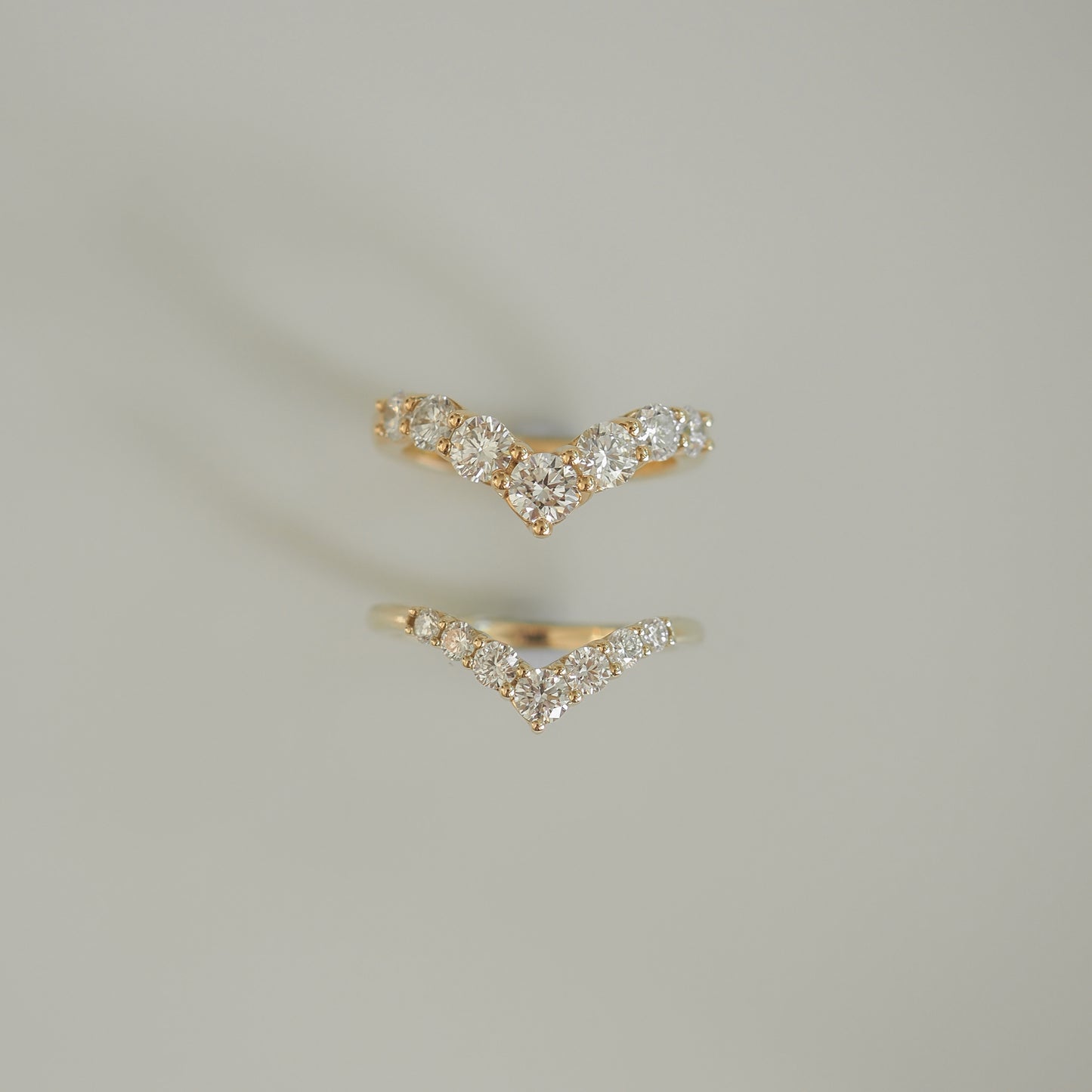 Two gold chevron rings with diamond accents on a light grey background, showcasing luxurious high-end jewellery craftsmanship.