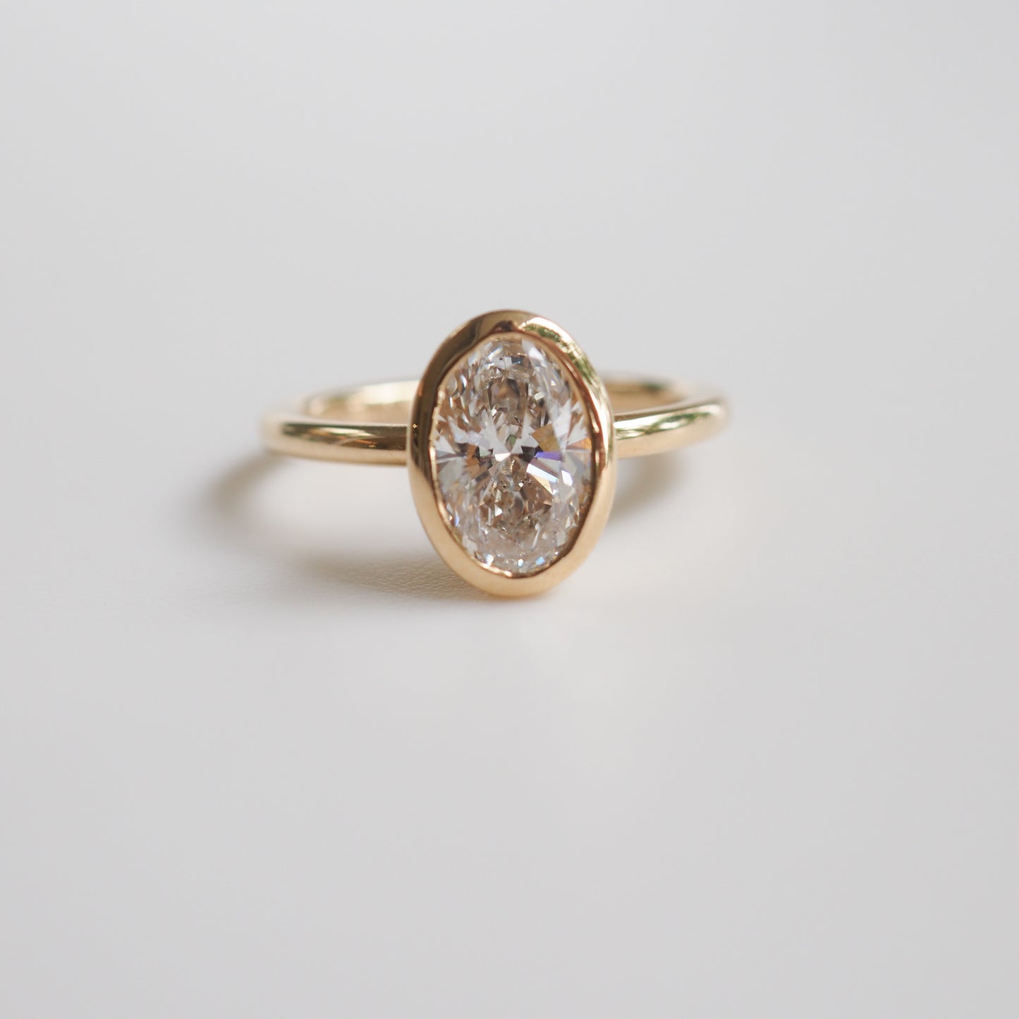 Gold ring with an oval-cut diamond in a bezel setting, displayed against a neutral background. Luxurious and elegant jewellery piece.