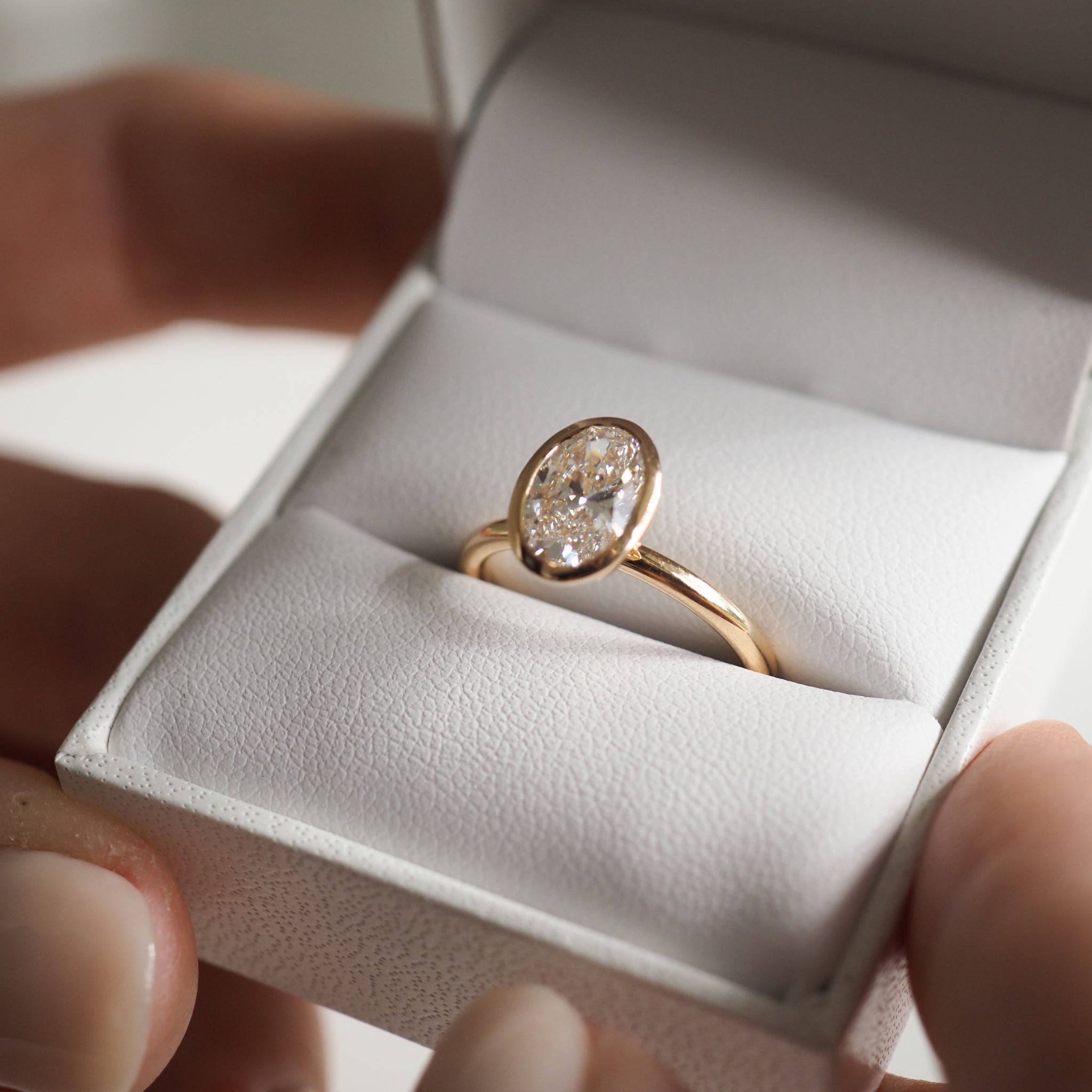 Gold engagement ring with oval diamond in an open jewellery box, held by hands. Luxurious and elegant presentation.