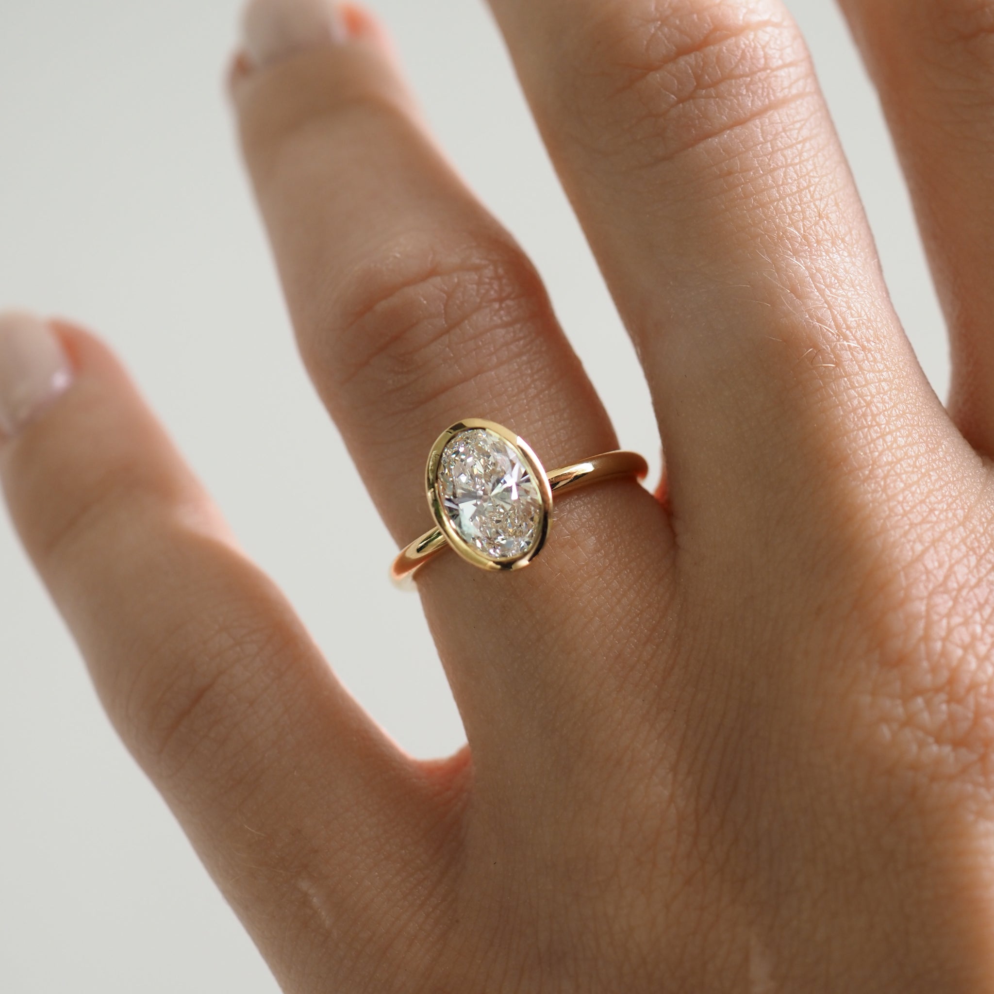 Close-up of a hand wearing a gold ring with an oval diamond setting. The jewellery piece exudes luxury and elegance.