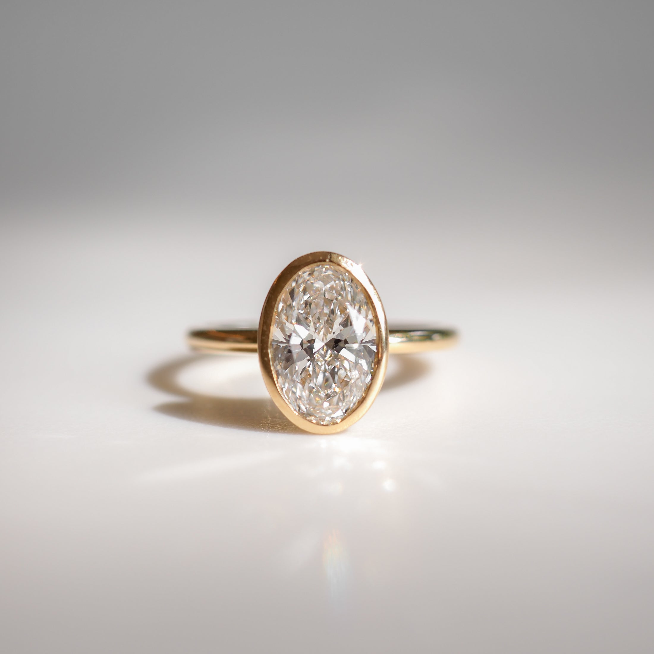 Gold ring featuring a prominent oval diamond, elegantly displayed on a reflective surface, evoking luxury and sophistication in fine jewellery.