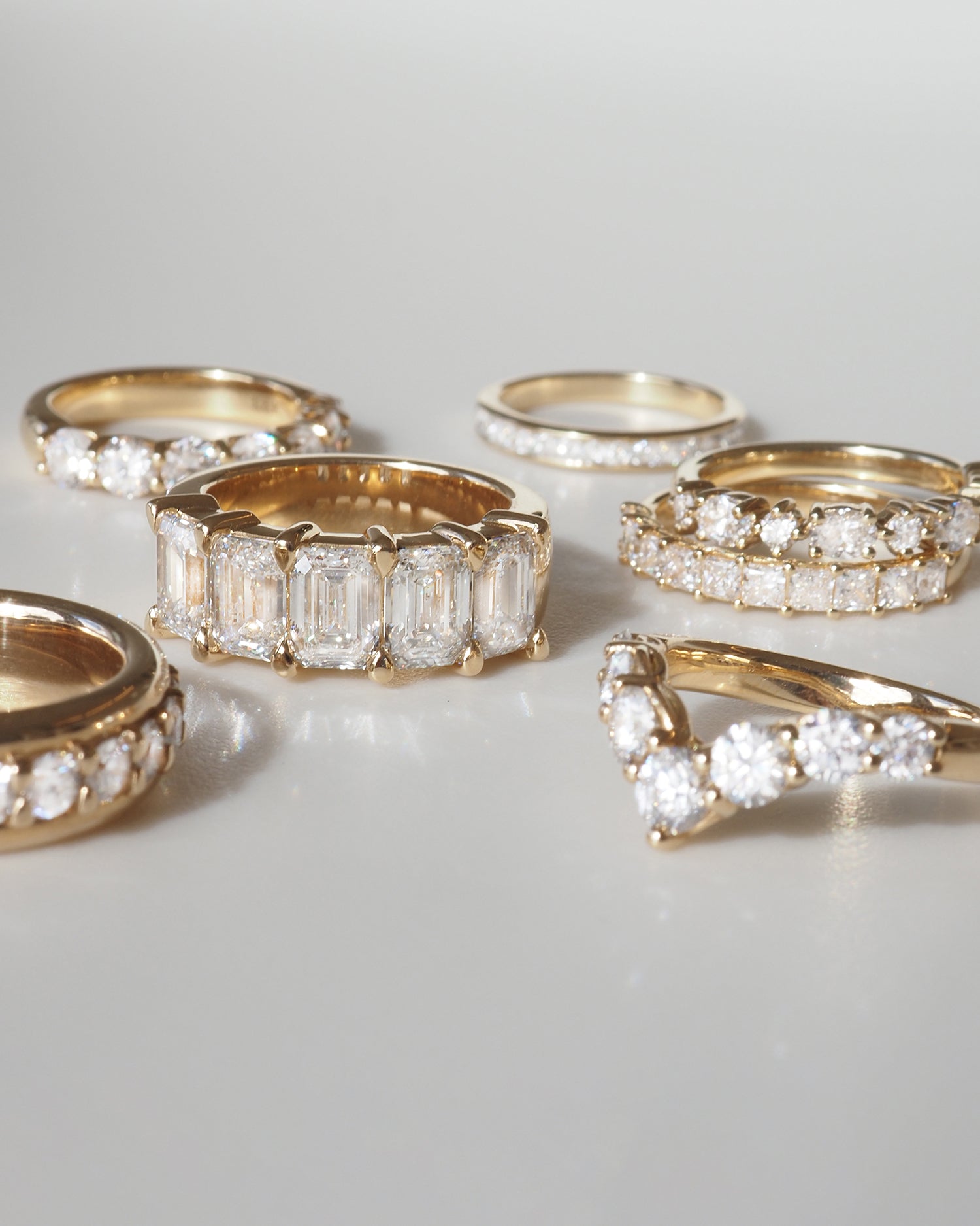 A collection of luxury gold rings featuring various diamond cuts, elegantly arranged on a reflective surface, highlighting their sparkle.