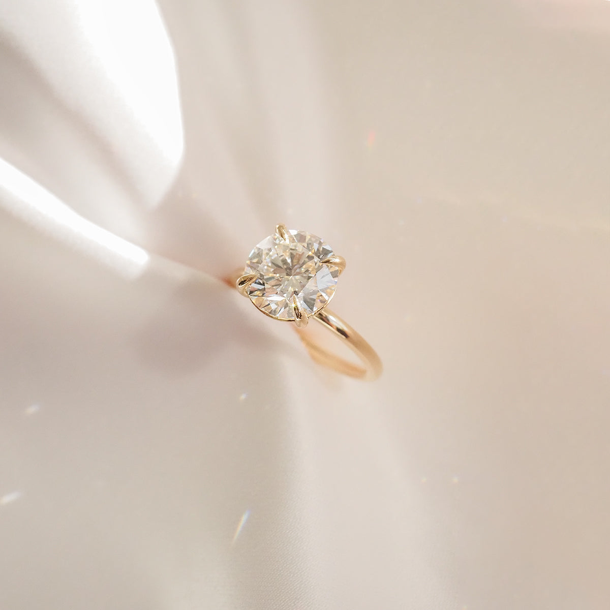 Gold engagement ring with a large round diamond, elegantly displayed on a reflective surface casting soft, radiant light patterns.