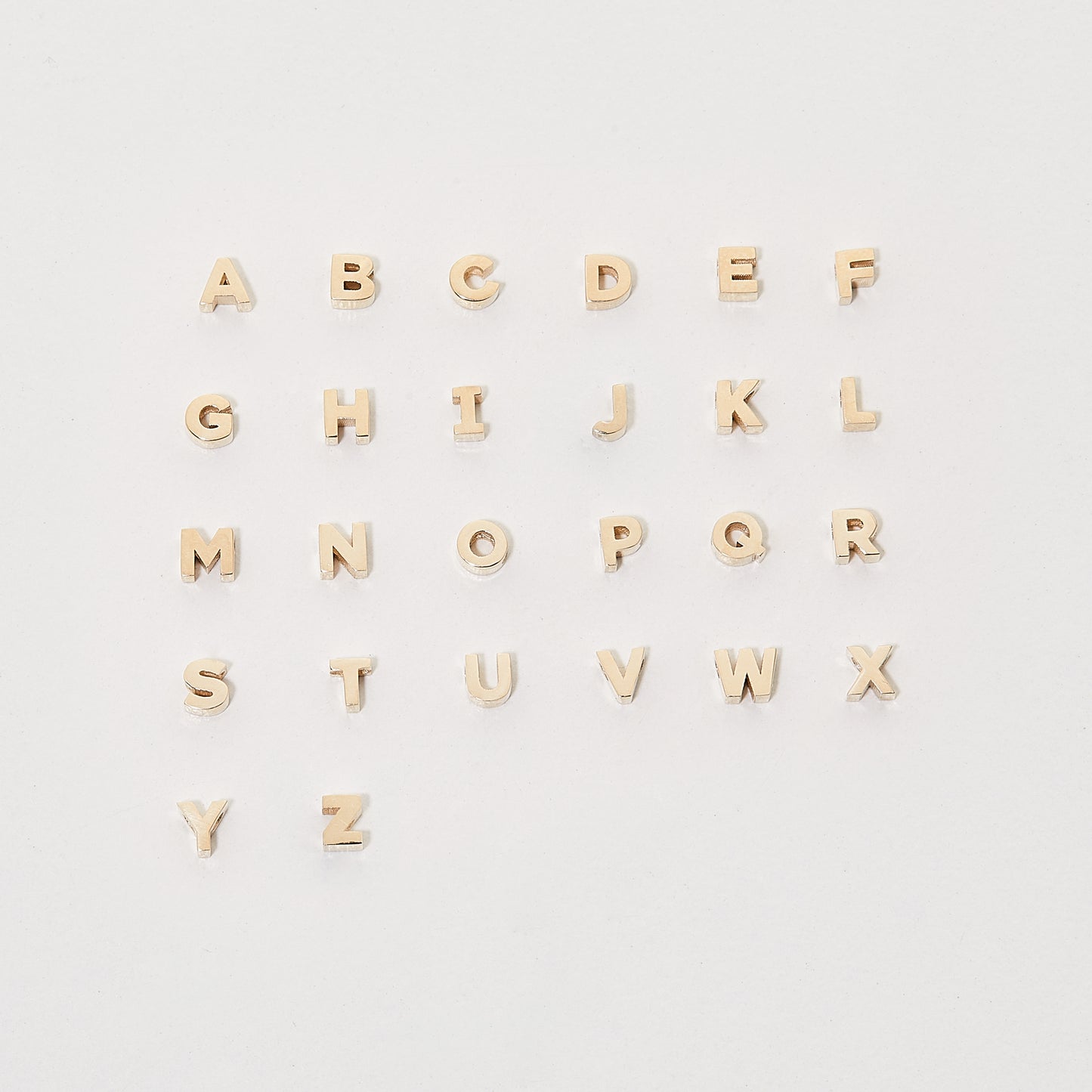 Gold alphabet letters arranged in four rows on a white background, showcasing luxury jewellery elements.