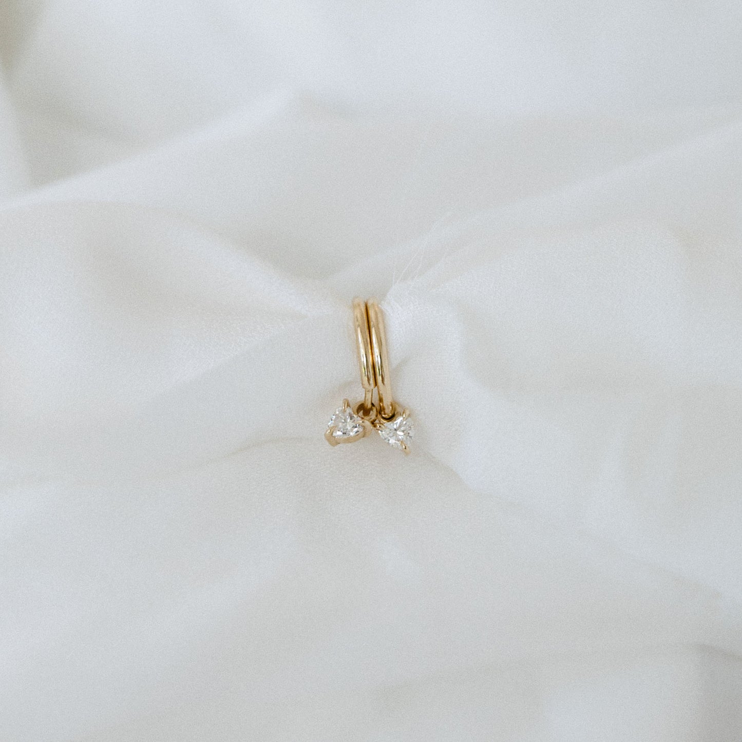 Gold hoop earrings with small diamonds on soft white fabric, showcasing luxury jewellery.