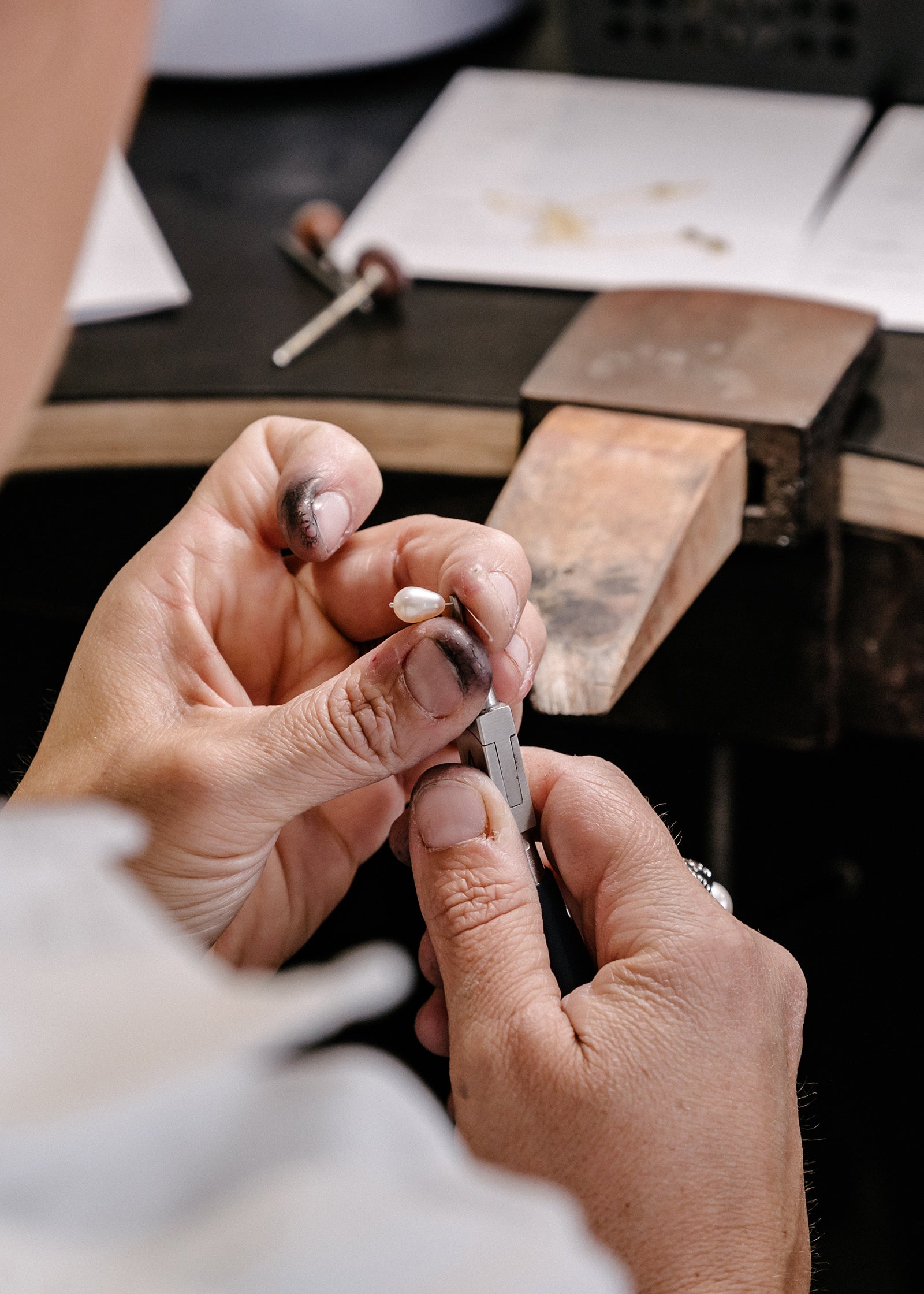 Jeweller's hands crafting a luxury piece with precision tools on a workbench, showcasing detailed artisanal jewellery craftsmanship.