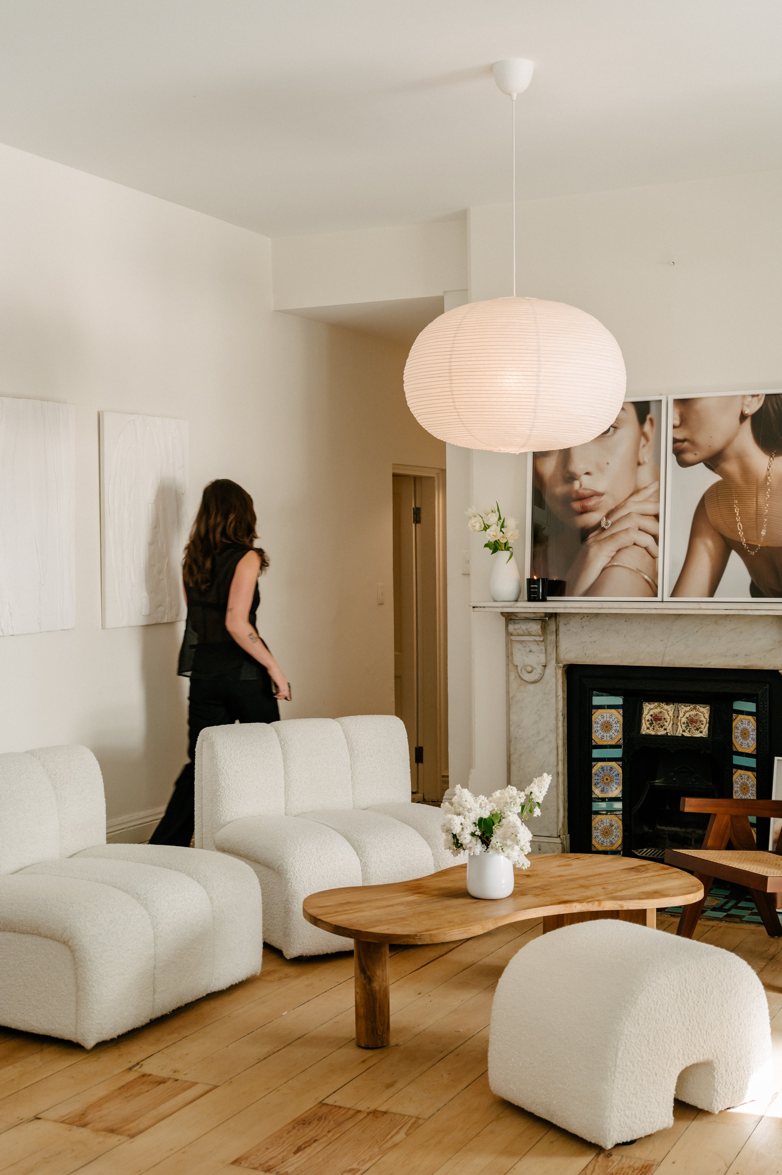 Elegant living room with modern white sofas, wooden table, and a pendant light. Jewellery artwork decorates the wall, adding a luxurious touch.