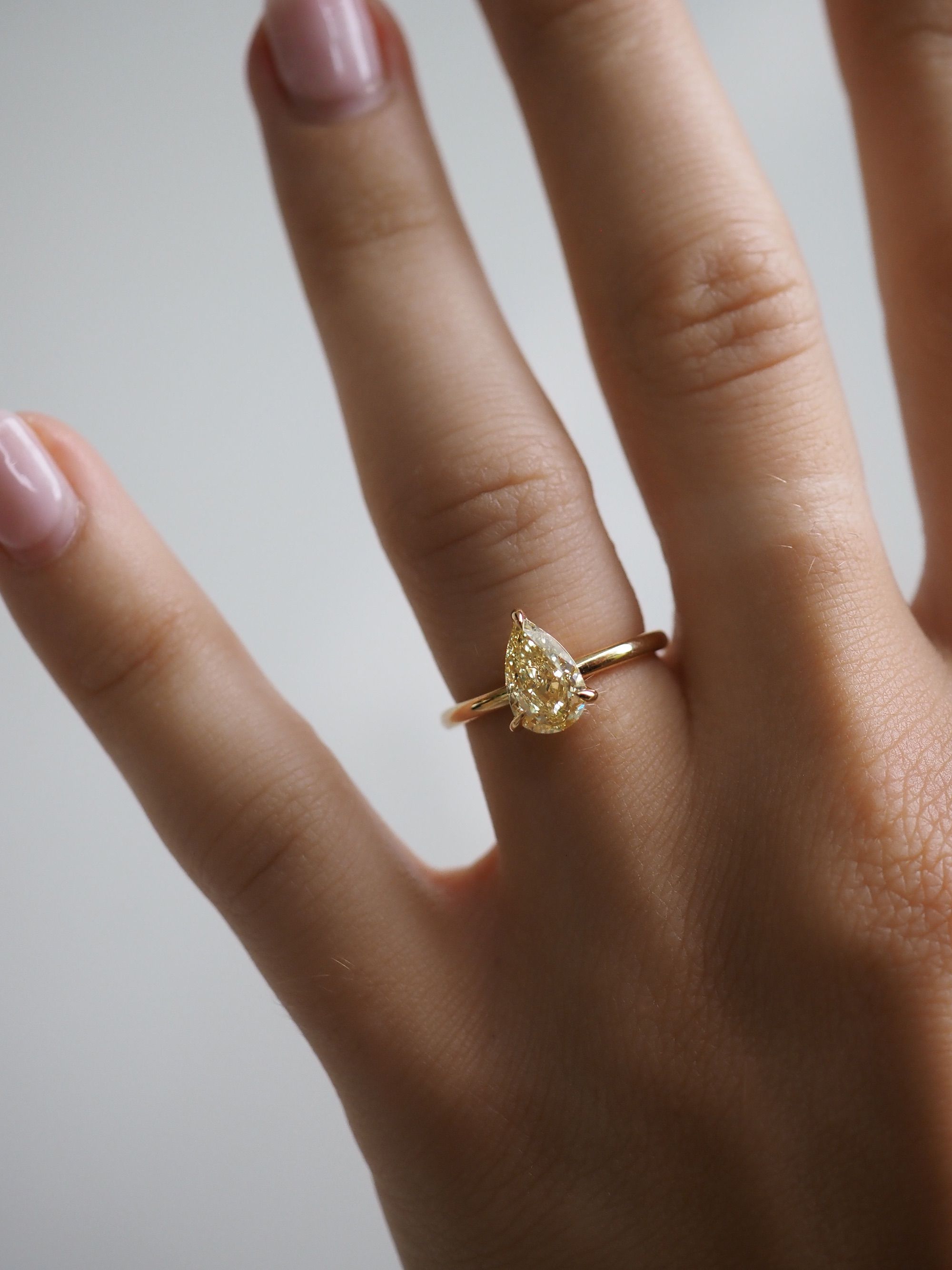 Pear-shaped diamond ring on a woman's finger with a gold band, showcasing elegance and luxury jewellery.