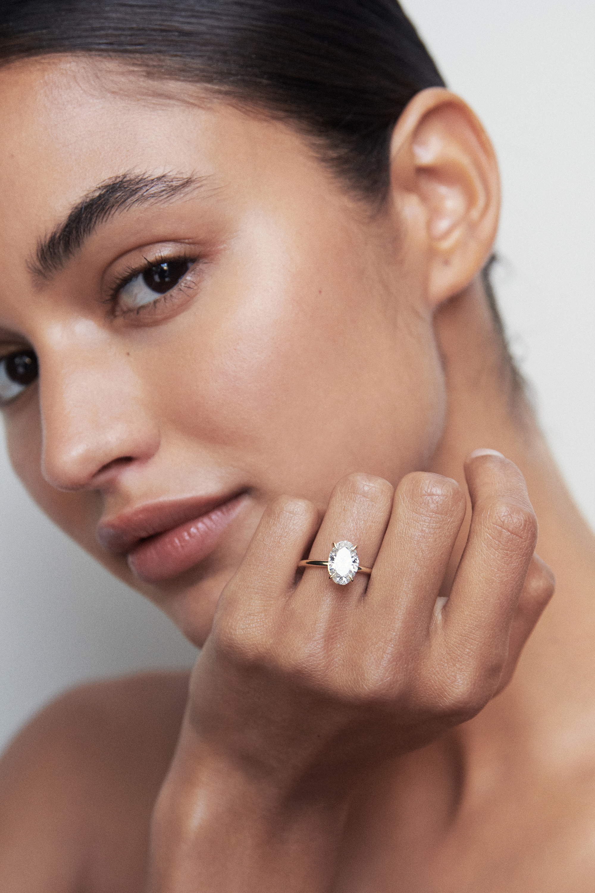 Woman showcasing an elegant, oval diamond ring on her finger, with a soft focus on her face highlighting luxury jewellery.