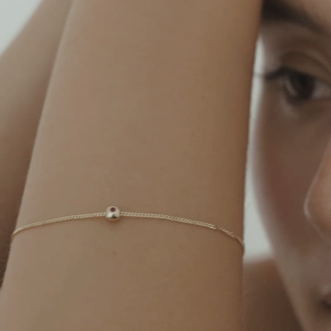 Video of a model wearing our 9ct Yellow Gold Tiny Birthstone Charm Bracelet with a personalised Ruby stone
