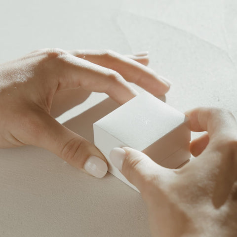 Model is opening our white leather ring box feauturing Ania.Our Ania ring showcases an oval centre stone shining between two smaller-sized pear shoulder stones. The ring pictured features a 1.00ct oval lab grown diamond and set in 18ct yellow gold. 