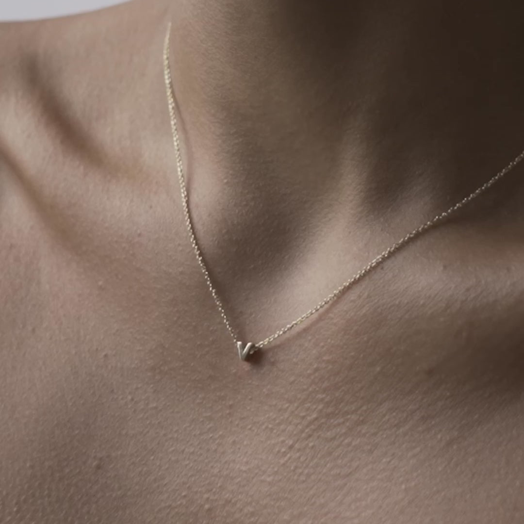 Solid gold and sterling silver jewellery: Close up video of a model wearing our signature 9ct yellow gold Tiny Letter V Charm Necklace on a 40cm cable chain