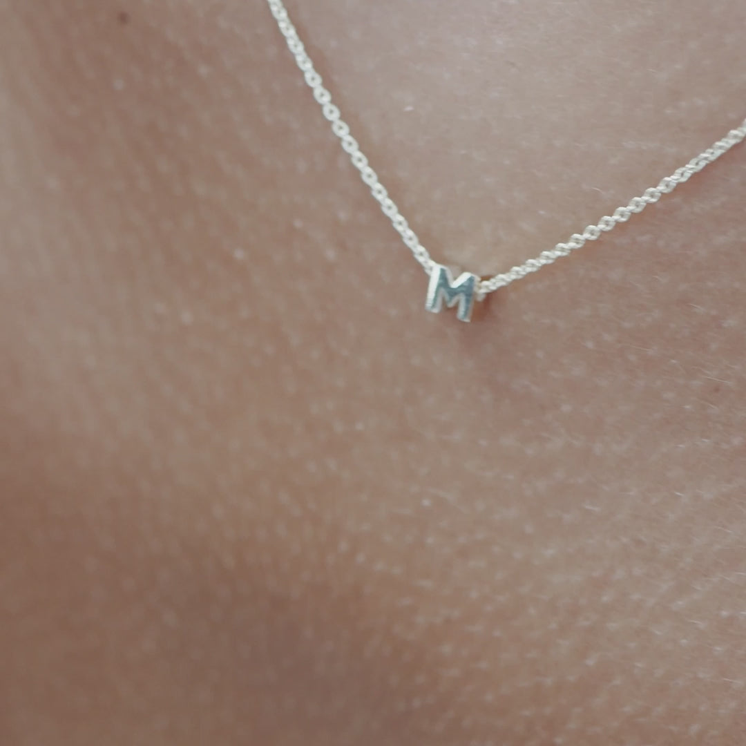 Solid gold and sterling silver jewellery: Close up video of a model wearing our signature sterling silver Tiny Letter M Charm Necklace on a 40cm cable chain