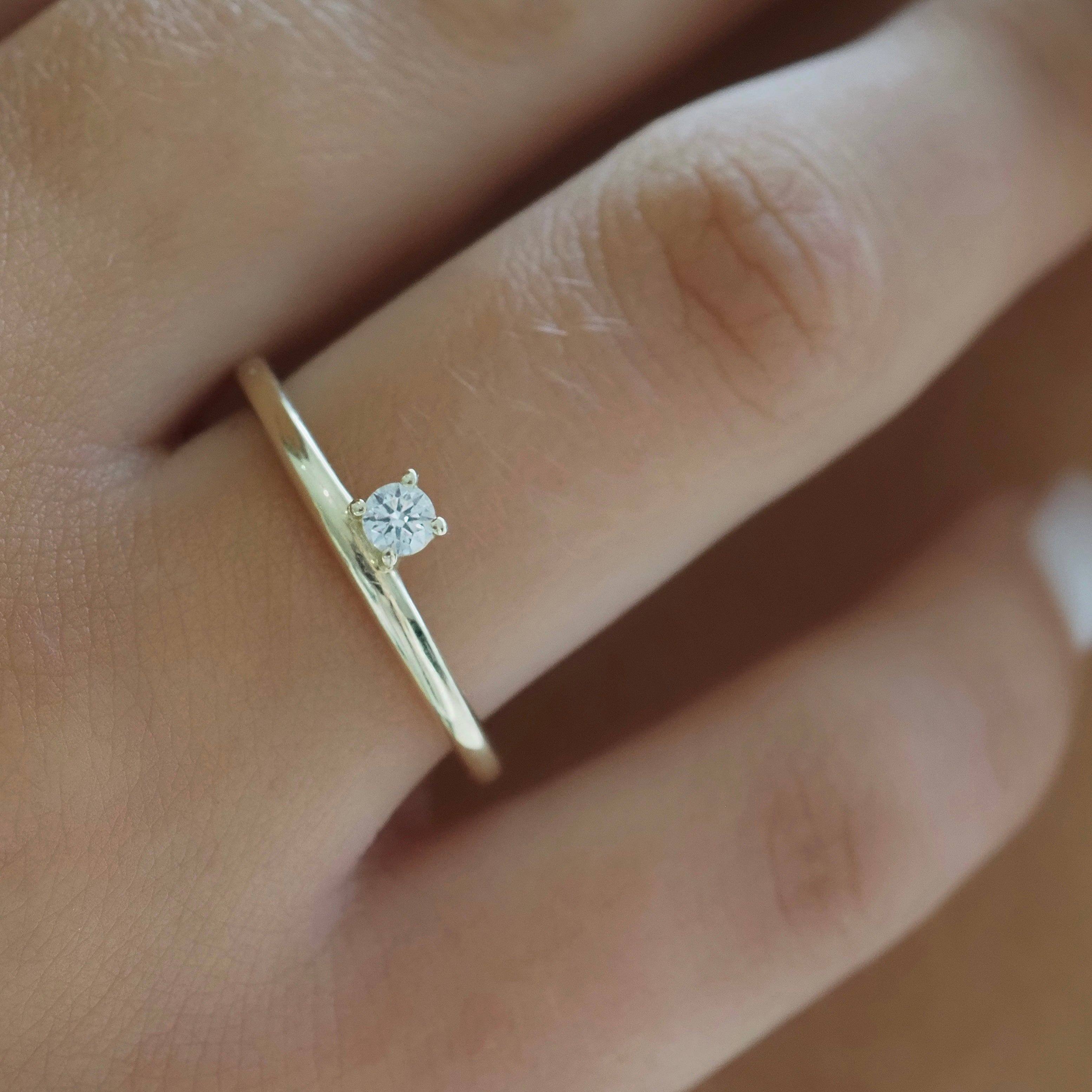 Gold solitaire ring with a round diamond on a woman's finger, showcasing minimalist luxury jewellery design.