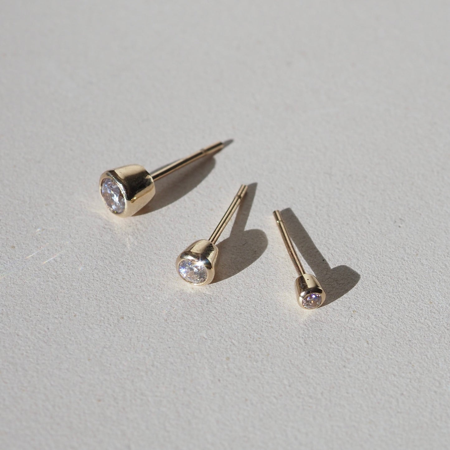 Three gold stud earrings with sparkling diamonds on a light surface, showcasing luxury jewellery craftsmanship in elegant simplicity.