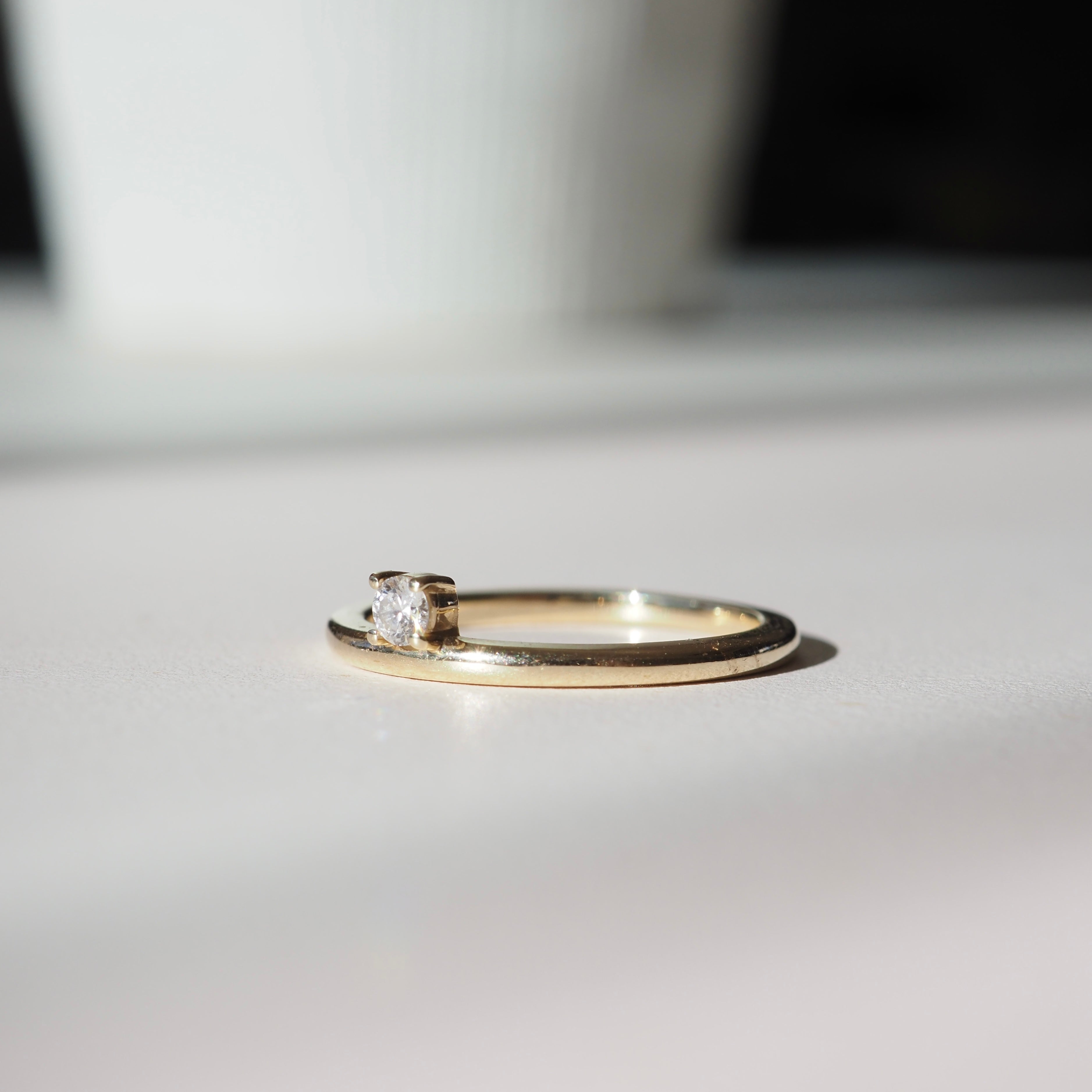 Gold ring with a single diamond setting placed on a smooth surface, softly lit, with a blurred background. Perfect luxury jewellery piece.