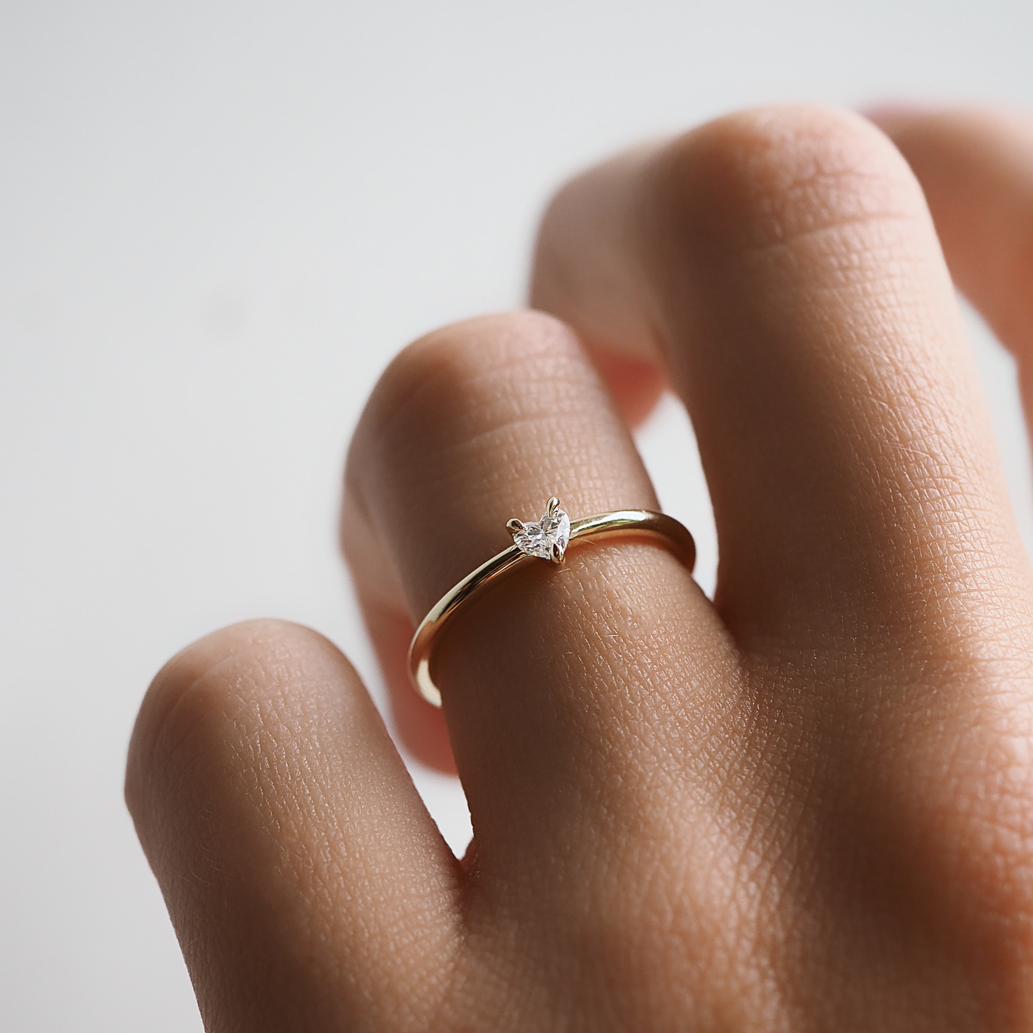 Close-up of a hand wearing a gold ring with a small, delicate heart-shaped diamond. Luxurious and elegant jewellery design.