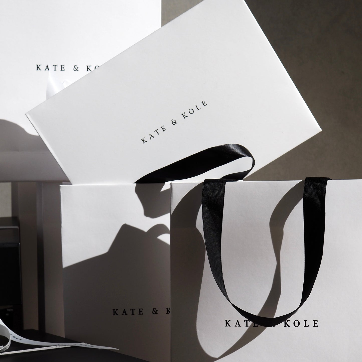 White gift bags with black "KATE & KOLE" branding and black handles are artfully arranged, embodying luxury jewellery packaging.