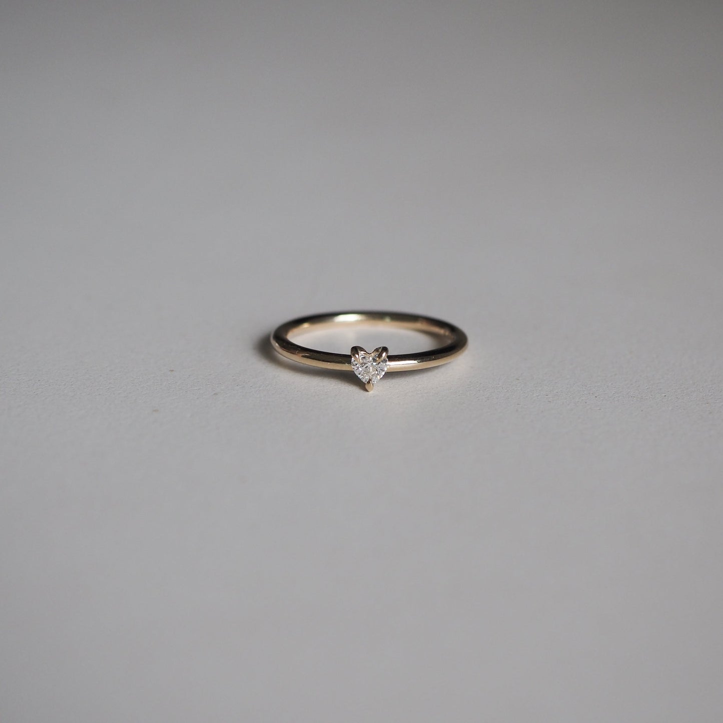 Elegant gold ring with a heart-shaped diamond on a minimalist grey background. Perfect for luxury jewellery lovers.