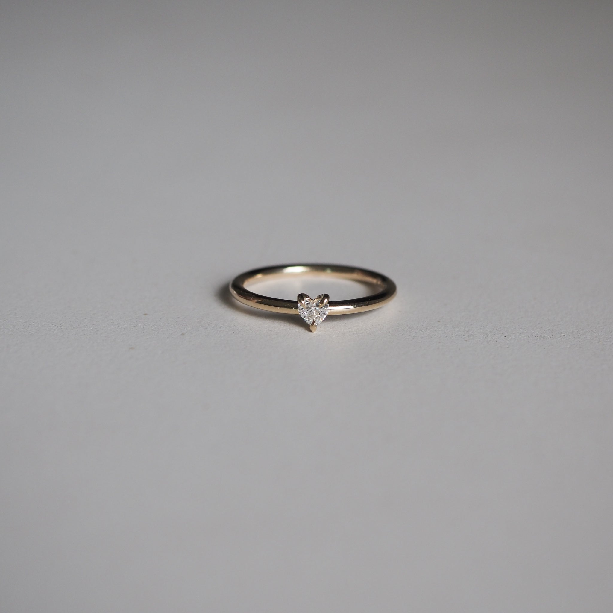 Elegant gold ring with a heart-shaped diamond on a minimalist grey background. Perfect for luxury jewellery lovers.